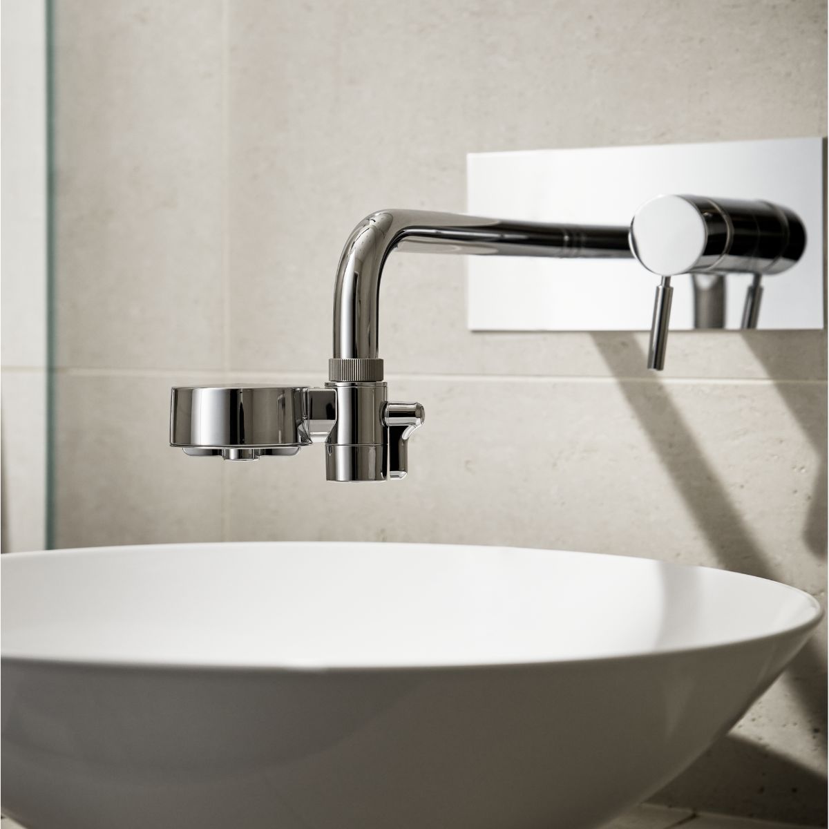 Chrome EcoPro Compact tap filter fitted to a wall-mounted tap above a round basin