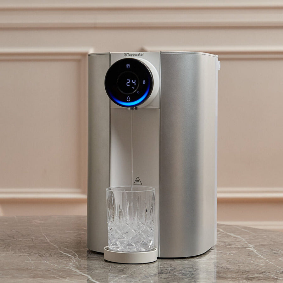 Tappwater benchtop reverse osmosis water filter on a marble bench, dispensing purified water into a crystal glass, display showing 24 degrees